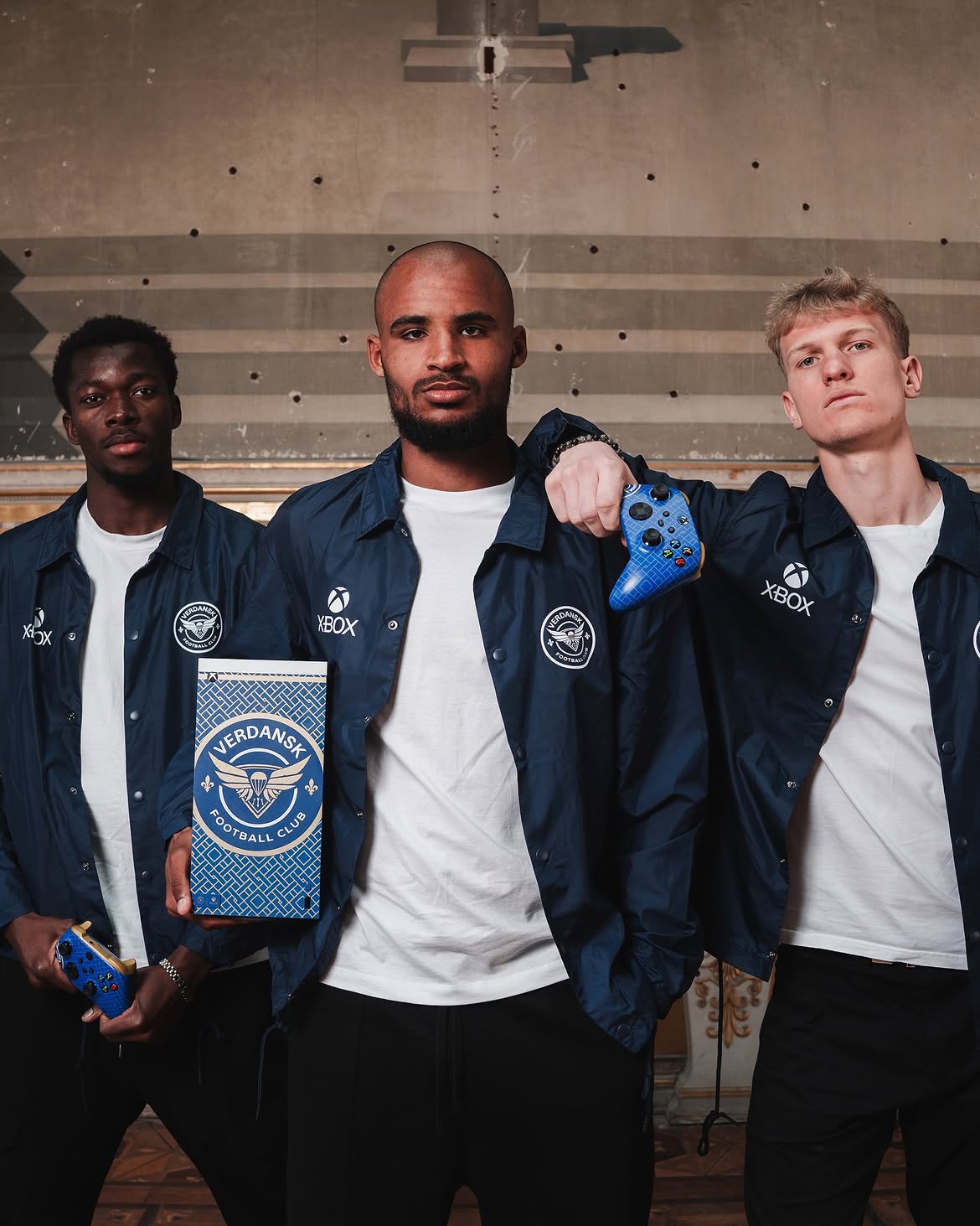 Three FC Versailles players in FC Verdansk jackets with the console and a controller